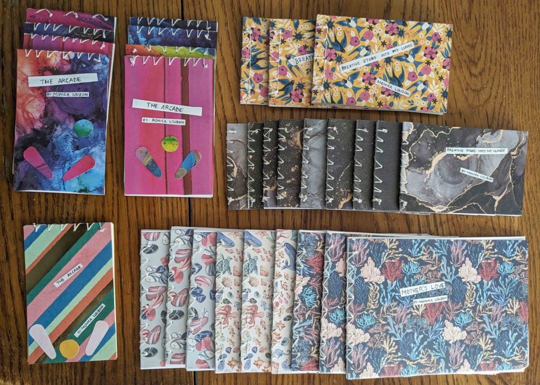 Picture of several handmade chapbooks with different covers and sizes. Some have stripes, some have sea creatures and undersea life, some have marble patterns, and some have pinball with pinball flippers over watercolor background.